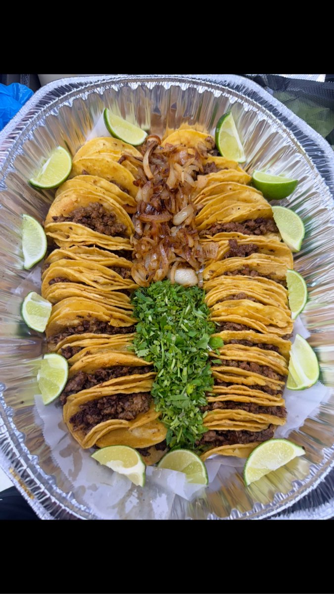 A large tray of street tacos with grilled onions, cilantro, and lime wedges
