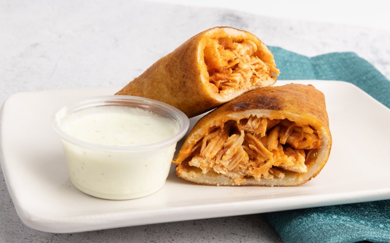 Chicken-filled empanadas cut open beside dipping sauce