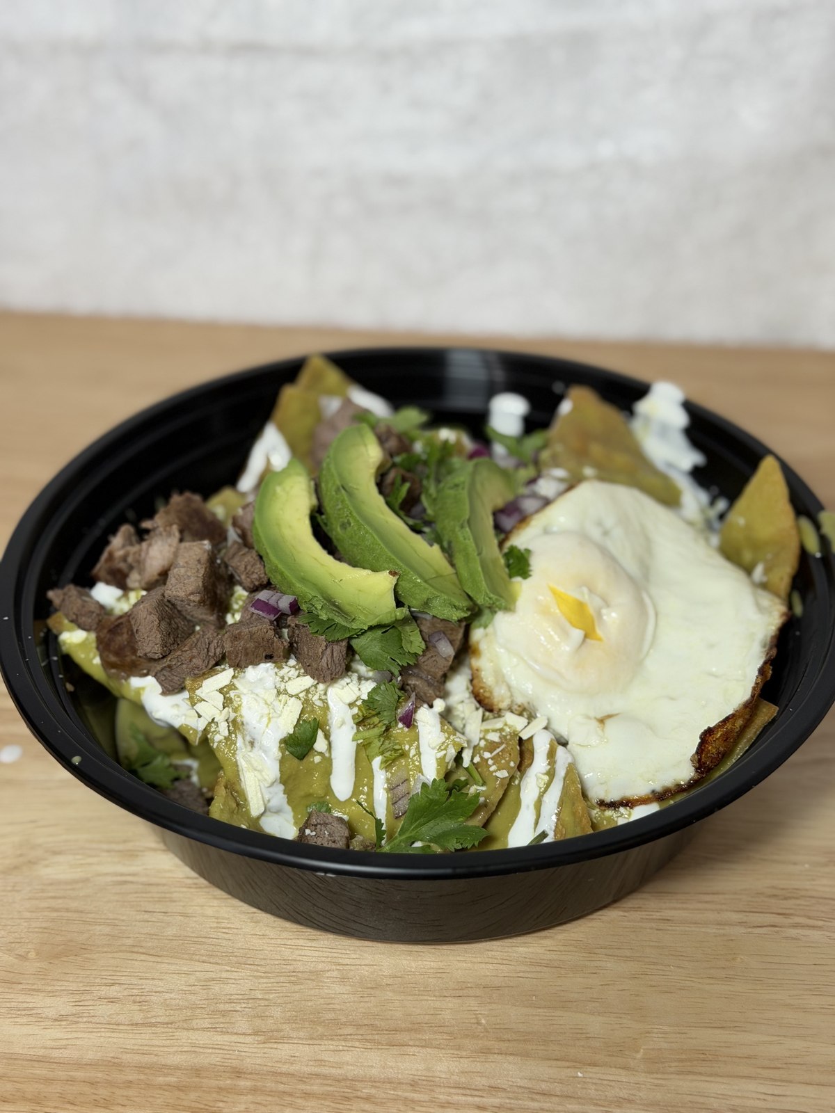 A bowl of chilaquiles verdes topped with steak, avocado, and a fried egg