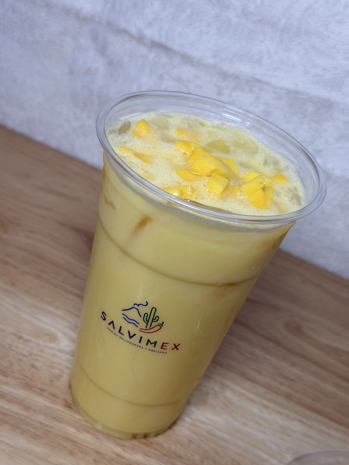 A cup of creamy mango agua fresca topped with fresh mango chunks